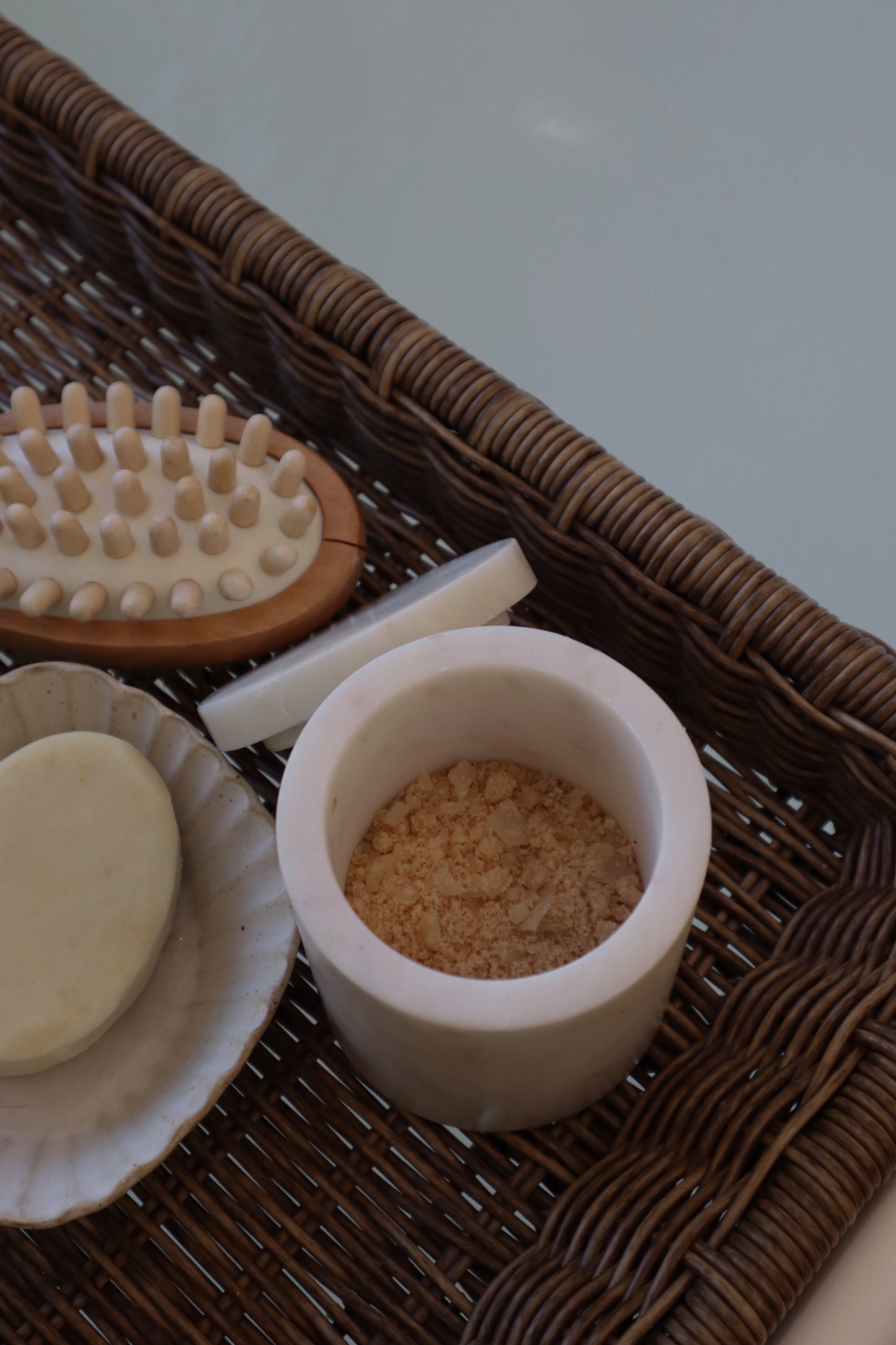 Assorted bath items including a brush, soap, and scrubber on a woven tray.