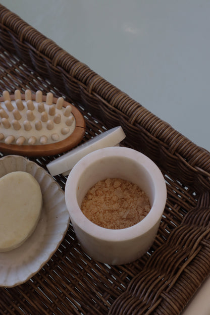 Assorted bath items including a brush, soap, and scrubber on a woven tray.