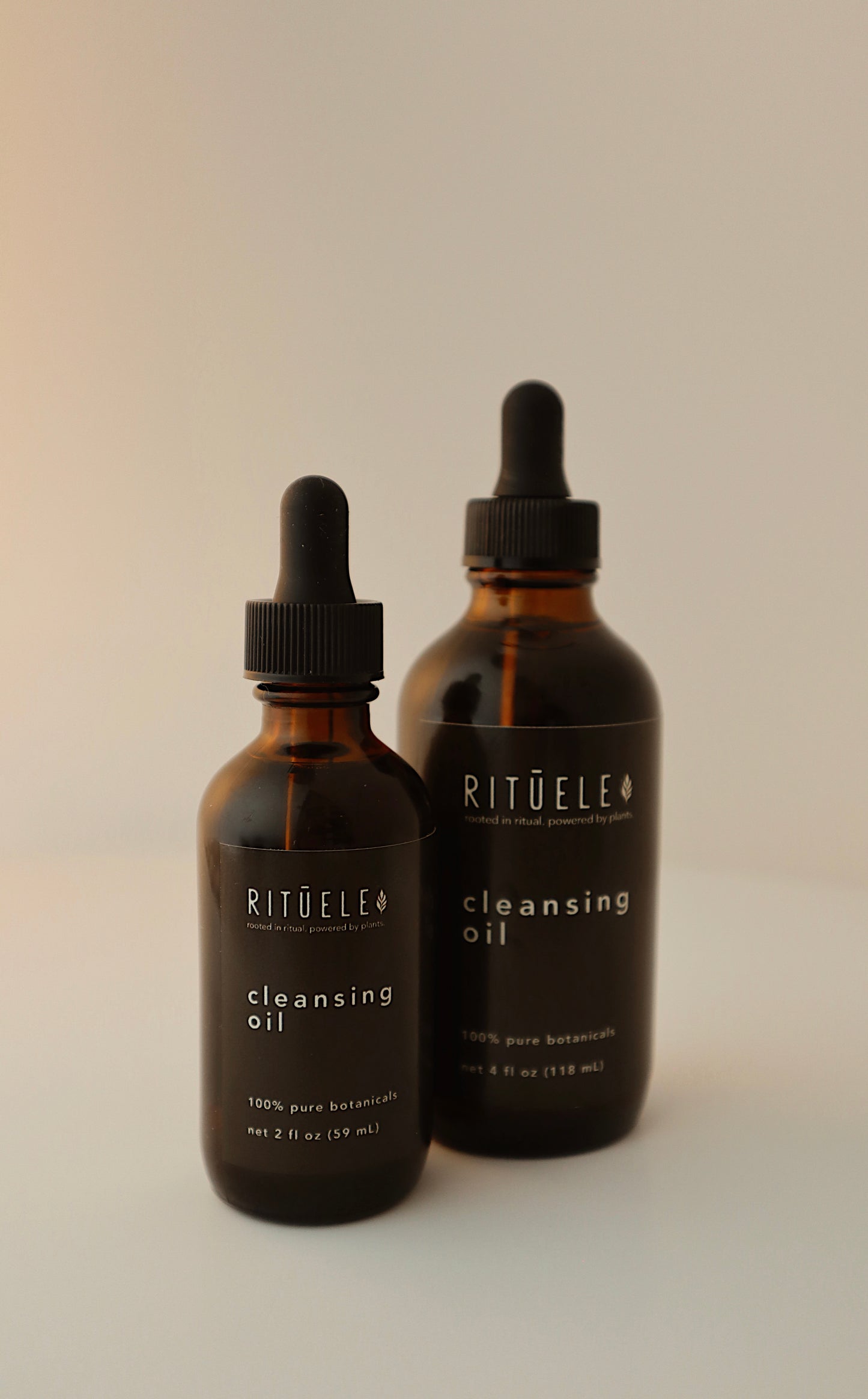Two bottles of ritūele cleansing oil on a neutral background