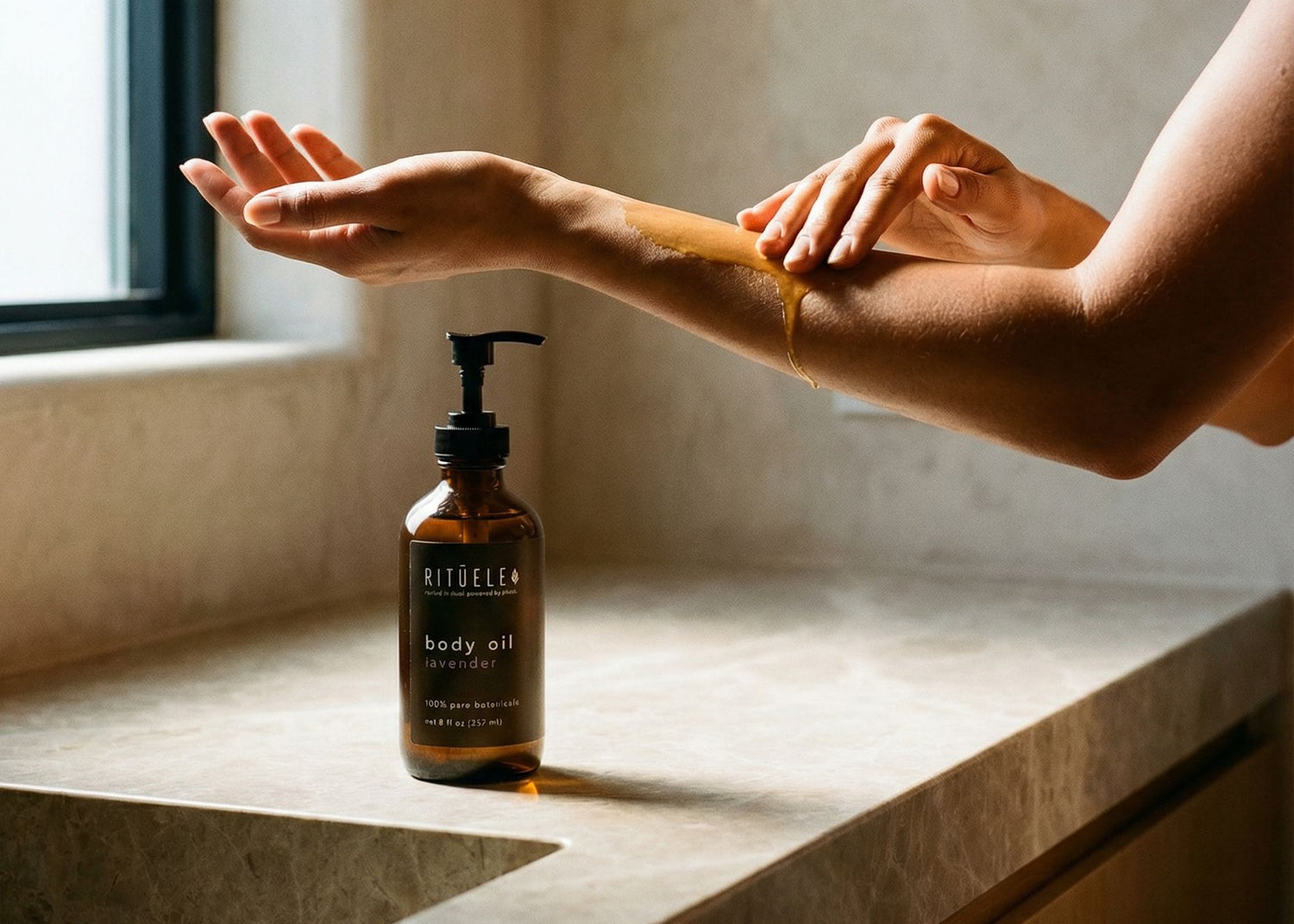 Person applying body oil to their arm with a bottle of body oil on a bathroom counter.