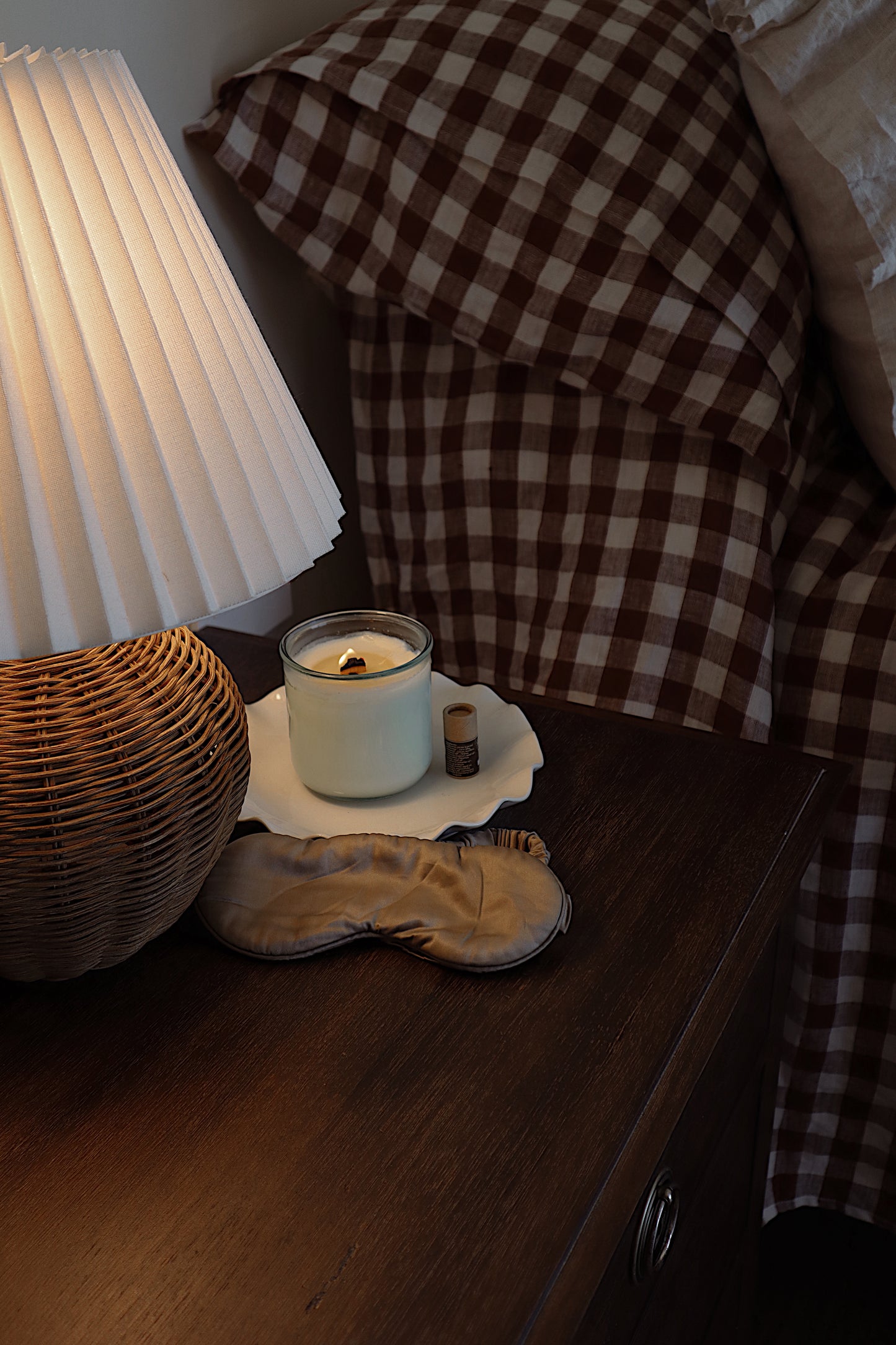 Candle on a nightstand next to a lamp and checkered blanket